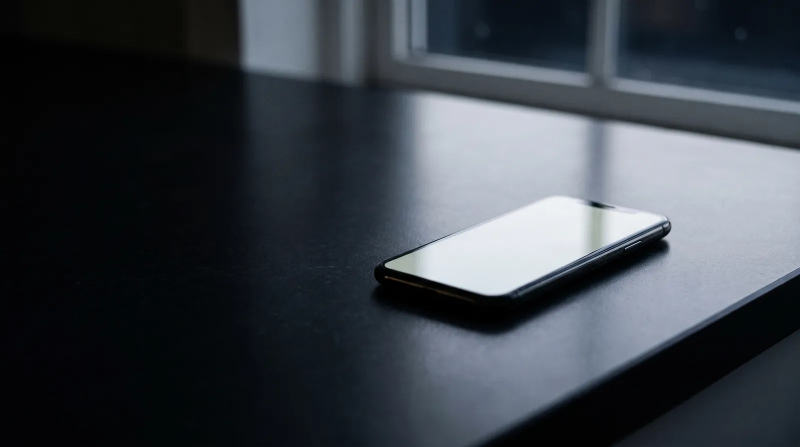 A phone with a blank lit screen on a dark kitchen counter at night, illustrative